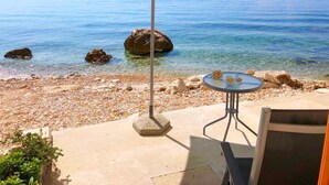 Una playa con una mesa y sombrilla, agua cristalina y rocas.
