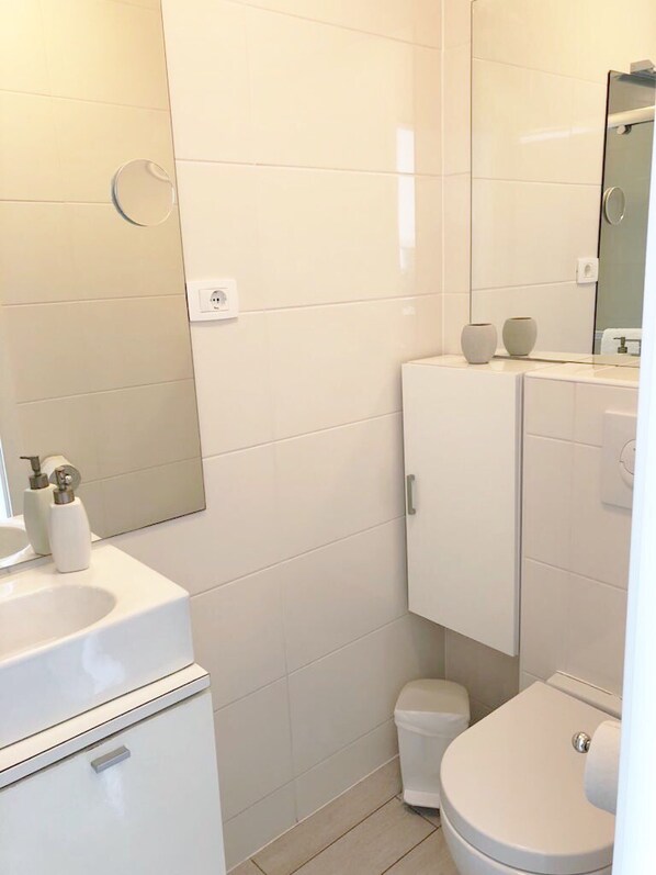 A modern bathroom with a white sink, toilet, and cabinet, and a mirror above the sink.