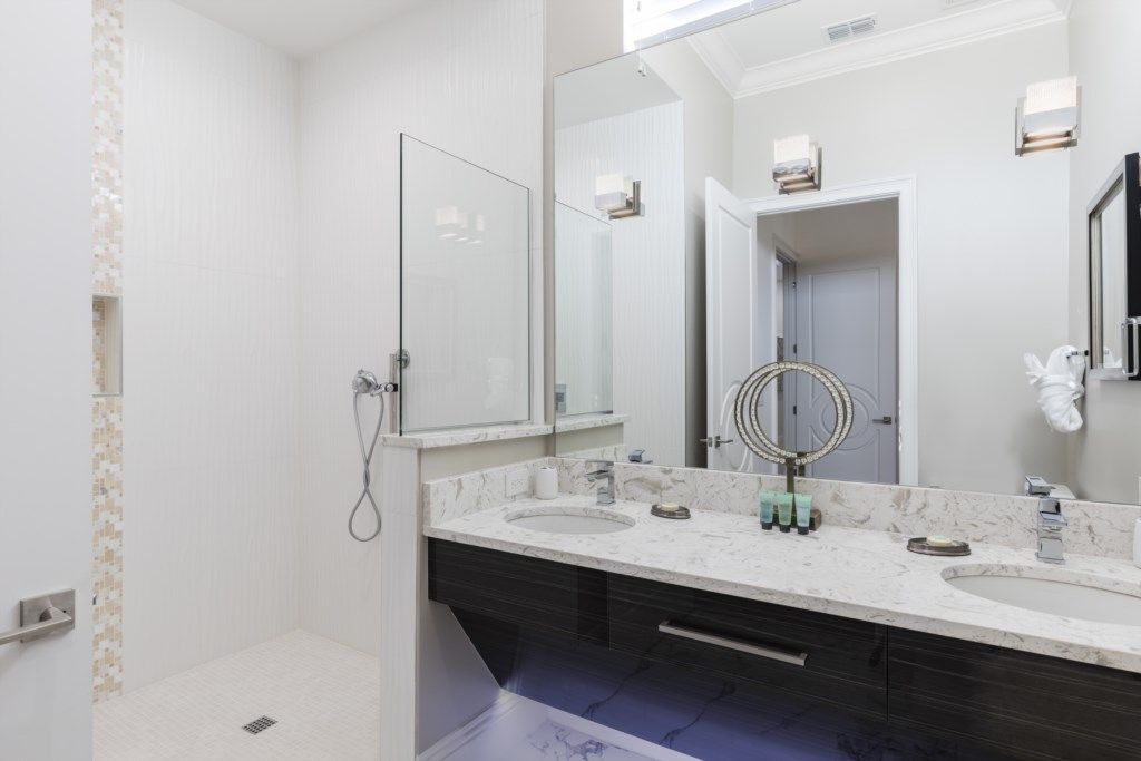 A modern bathroom with a large mirror, two sinks, and a shower.