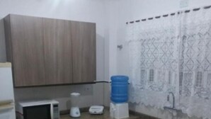 Una pequeña cocina con microondas, tostadora y dispensador de agua sobre la encimera. Hay un lavabo y armarios debajo.