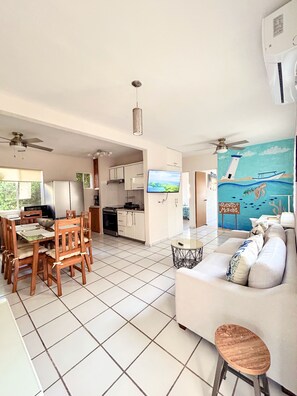 A modern living space with a dining area, kitchen, and a mural of a coastal scene.