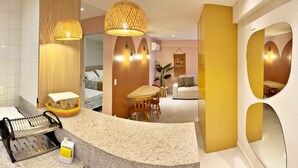 A modern hotel room with a curved marble counter, a dining area with a wooden table and chairs, a sofa, and a large mirror with circular cutouts. - Vacanze - edf. Port Ville III apt 309, rooftop pool with panoramic views. (Maceió)