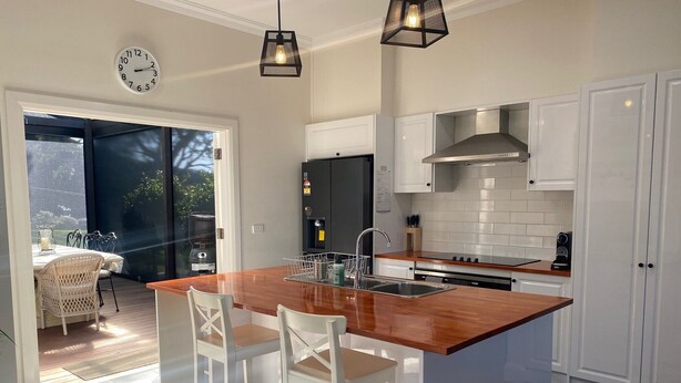 Una cocina moderna con una isla central, taburetes blancos de bar, un lavamanos empotrado y vistas a un patio exterior.