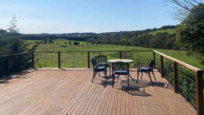 Una terraza de madera con mesa y sillas con vista a un paisaje verde.