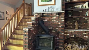 Una sala de estar con chimenea de ladrillo, una escalera de madera y un cuadro enmarcado en la pared.