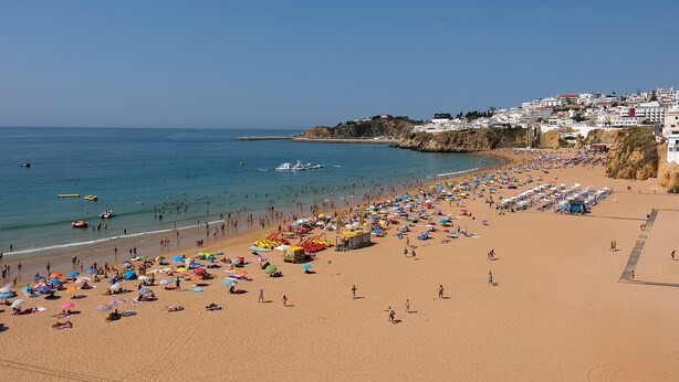 A beach with umbrellas and people, a clear sky, and buildings in the background. - Lotus Villa, Praia da Ora - Albufeira (Albufeira)