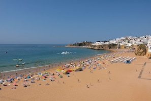 A beach with umbrellas and people, a clear sky, and buildings in the background.