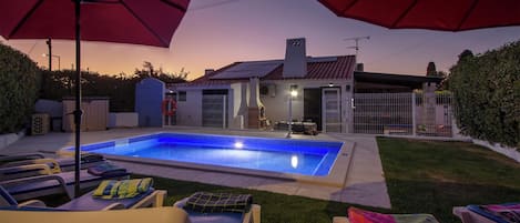 A backyard with a swimming pool, lounge chairs, and umbrellas.