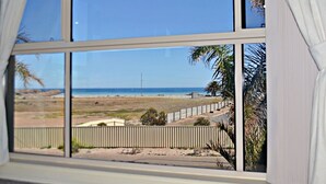 A view from a window overlooking a beach with a fence and palm trees. - 'The Shack' Copper Cove Marina - Only Steps to North Beach (Wallaroo)