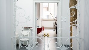 A doorway with a white metal frame leading to a room with a red chair, a wooden cabinet, and a lamp.