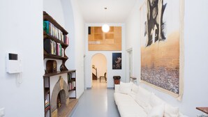A modern living room with a white sofa, a bookshelf, and a large painting on the wall.