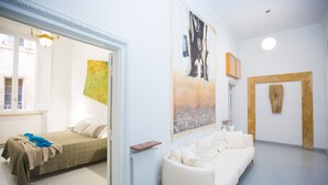 A room with a bed, a white sofa, and two paintings on the wall.