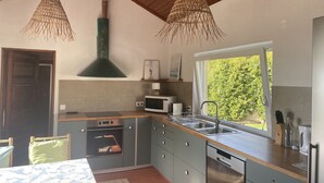 Une cuisine moderne dotée d’un four, d’un micro-ondes et d’un lave-vaisselle encastrés, d’un plafond en bois et d’une grande fenêtre offrant une vue sur la verdure.