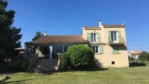 Une maison à deux étages, avec un toit recouvert de tuiles, des volets verts et un petit balcon.