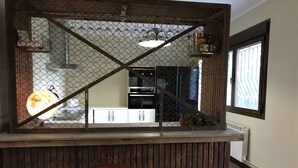 A bar area with a wooden counter, a stool, and a view of a kitchen through a wire mesh partition. - Casa de Campo el Encinar - Paddleball, Pickleball, Swimming Pool and Barbecue (Santa Cruz del Retamar)