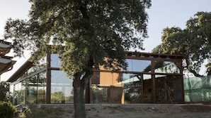 A modern building with large glass windows, a wooden structure on the roof, and a tree in the foreground. - Casa de Campo el Encinar - Paddleball, Pickleball, Swimming Pool and Barbecue (Santa Cruz del Retamar)