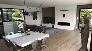 A modern living room with a dining area, a television, and a fireplace. - Architect Villa with heated pool  (Séné)