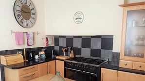 Une cuisine avec des meubles de rangement en bois, un plan de travail noir, une cuisinière et une horloge au mur.