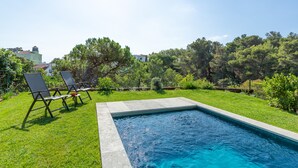 Una piscina con dos sillas de descanso, rodeada de césped y árboles.