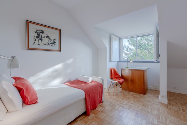 Un dormitorio moderno con una cama blanca, almohadas rojas, un escritorio de madera y un ventanal grande.
