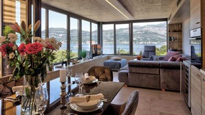 A modern living room with a dining area, large windows, and a view of the sea.