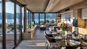 A modern dining area with a view of the sea, large windows, and contemporary furniture.