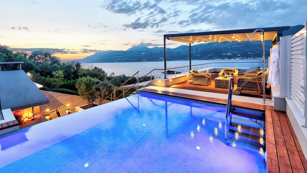 A swimming pool with a view of a lake and mountains at dusk.