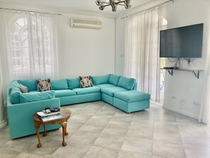 Un salon avec un canapé d’angle de couleur turquoise, une table basse en bois et un téléviseur à écran plat fixé au mur.