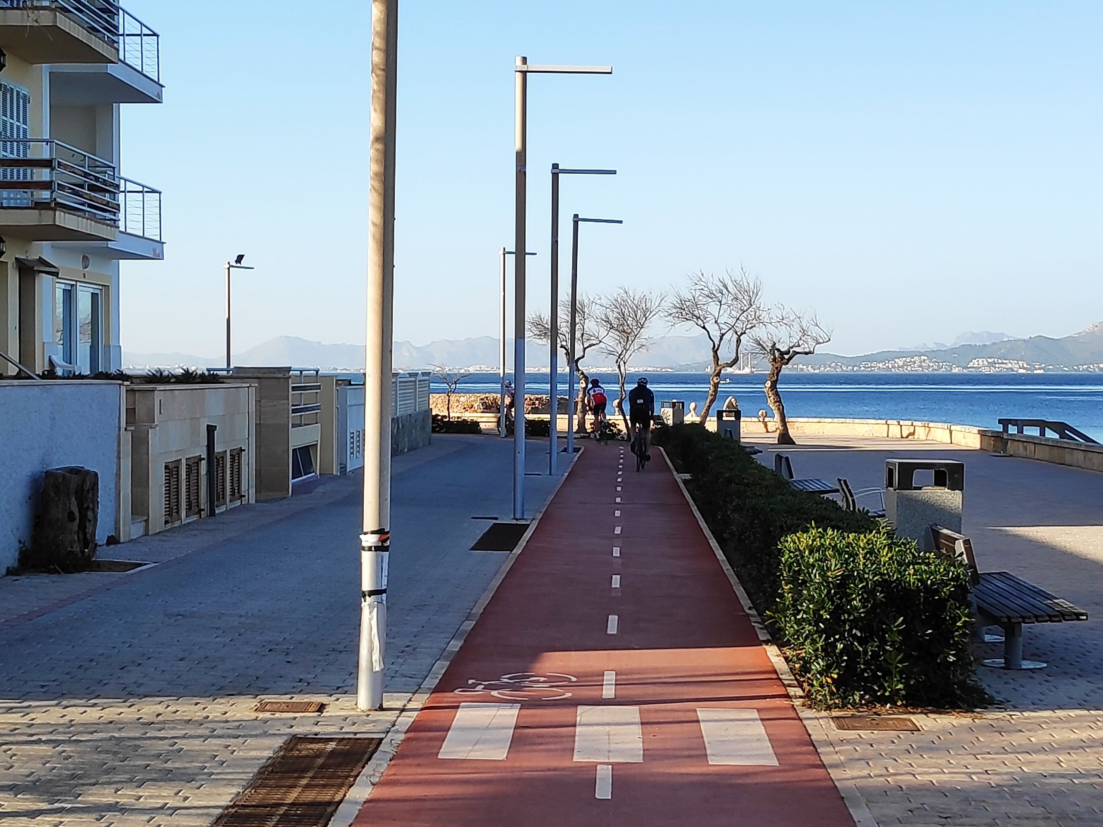 Une promenade en bord de mer avec une piste cyclable rouge, des bancs et des lampadaires.