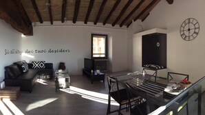 A living room with a black sofa, a glass coffee table, a TV, and a wall clock.