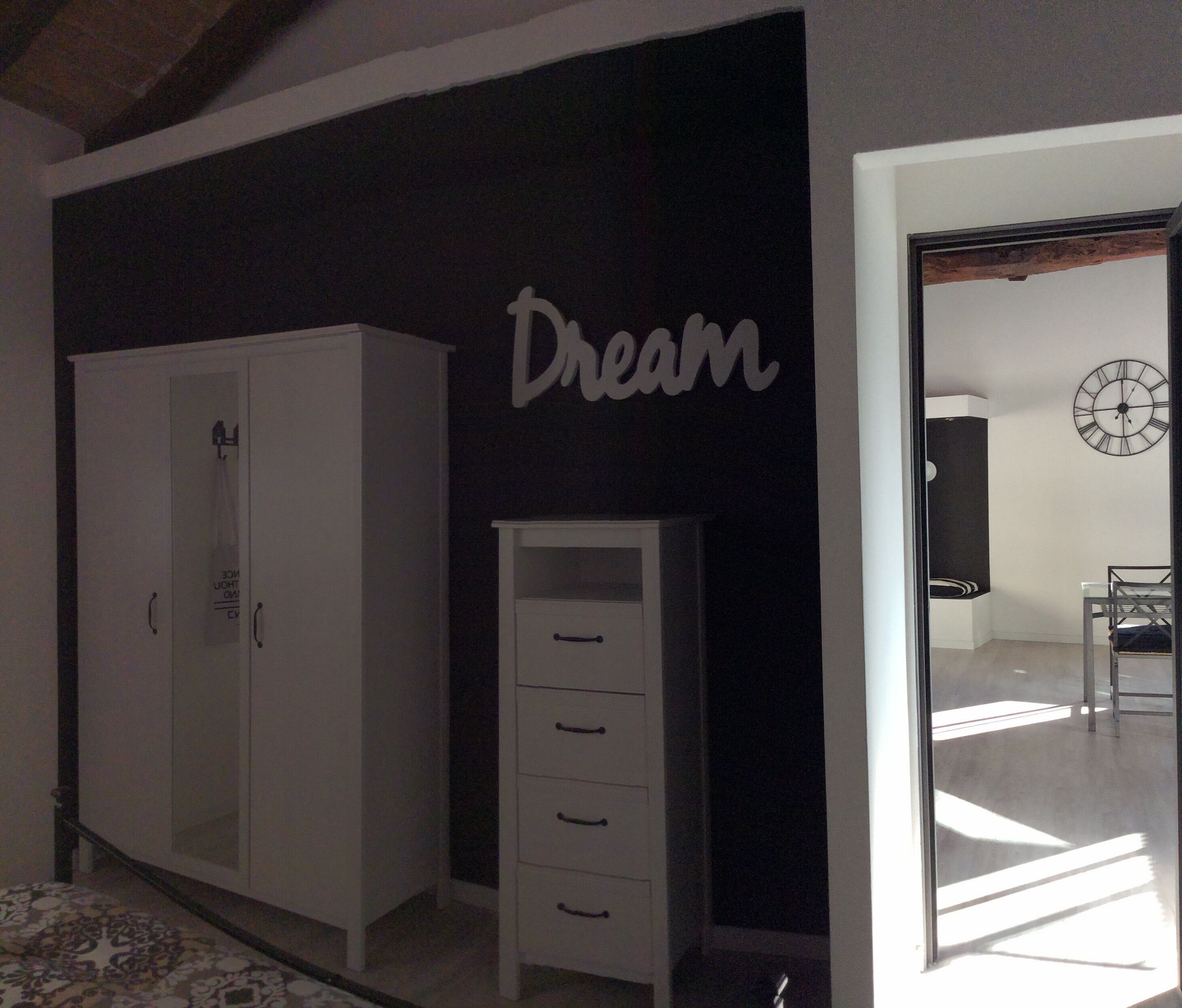 A bedroom with a wardrobe, a small cabinet, and a wall clock.