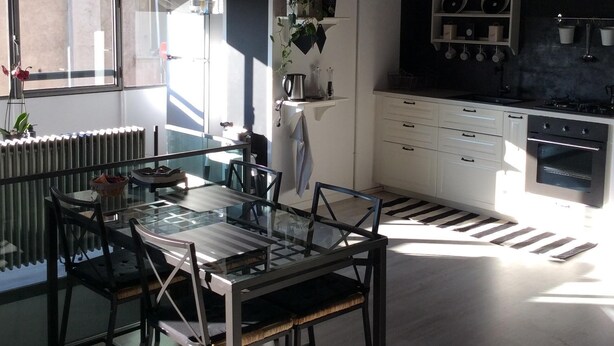 A modern kitchen with white cabinets, a black countertop, and a built-in oven. There is a dining area with a glass table and chairs.