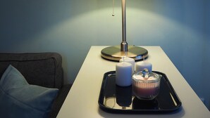 Een moderne kamer met een witte nachtkastje, een lamp, en een dienblad met kaarsen en een glazen vaas.