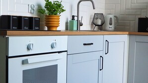 Een keuken met witte kasten, een houten aanrecht, een fornuis, een spoelbak en een koffiezetapparaat.