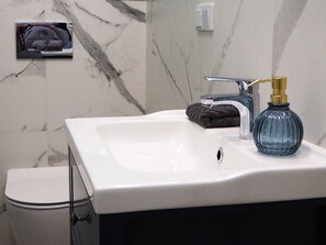 A bathroom with a white sink, a towel, a soap dispenser, and a toilet. - Wawelove Kossak Spacious 2 Bedroom Apt. (Kraków)
