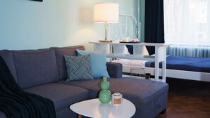 Een moderne woonkamer met een bank, een salontafel en een lamp. Er staat een bed met een blauwe sprei en een raam met gordijnen.