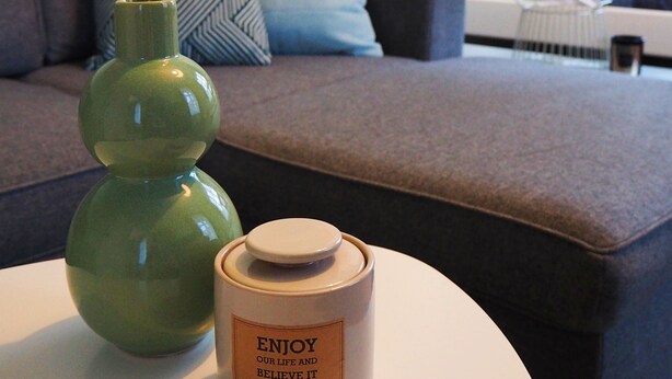 Een moderne hotelkamer met een bank, een groene vaas en een geurende kaars op een ronde tafel.