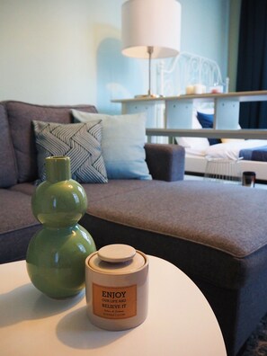 Una habitación de hotel moderna con un sofá, un jarrón verde y una vela aromática sobre una mesa redonda.