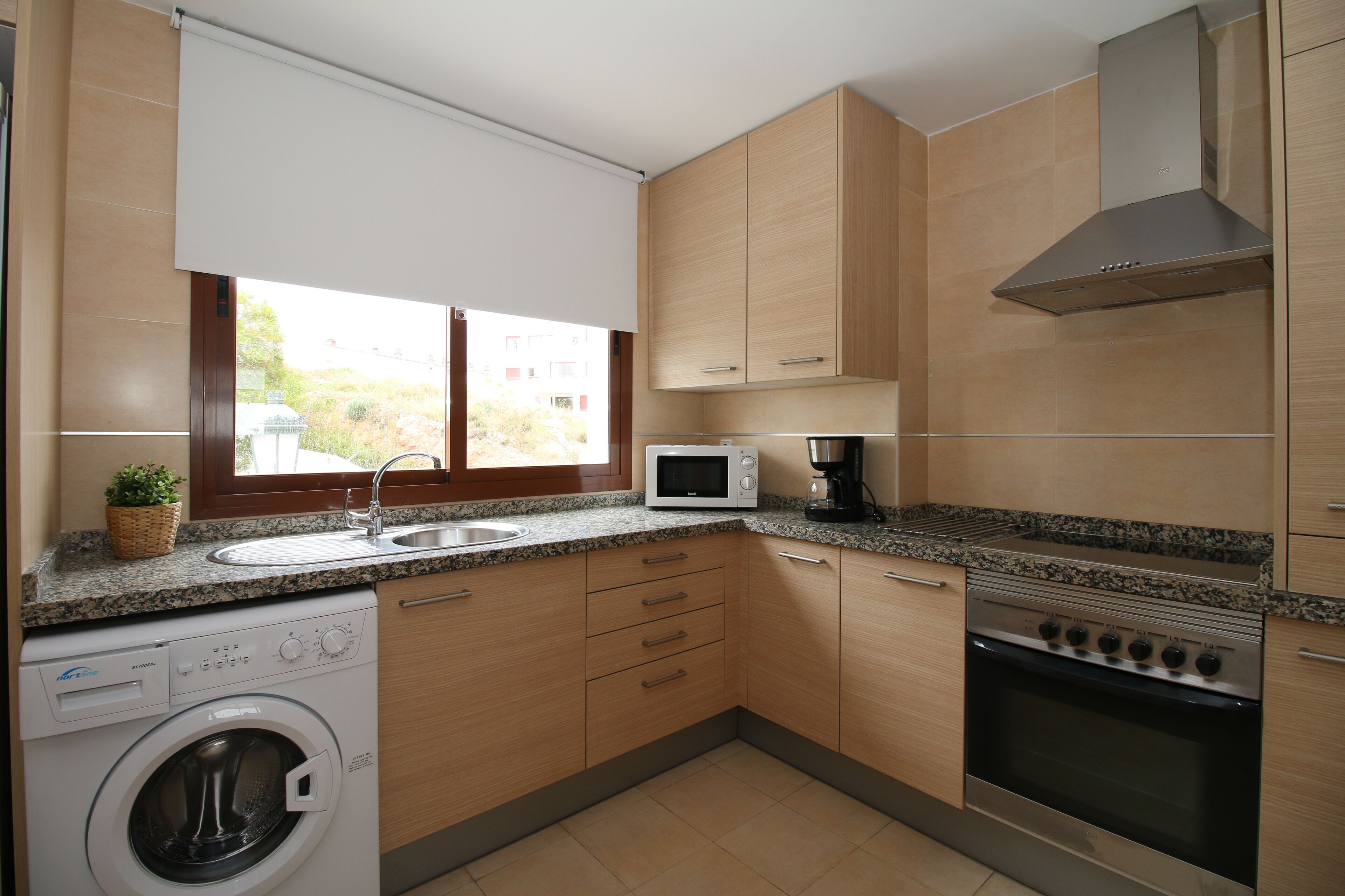 A compact kitchen with a washing machine, microwave, stove, and wooden cabinets.