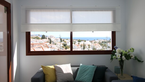 Ein Zimmer mit großem Fenster und Blick auf eine Stadtlandschaft, einer Couch mit Kissen und einer Vase mit Blumen.