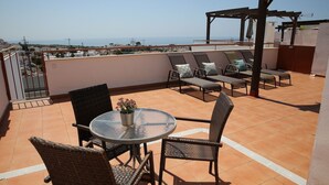 Eine Dachterrasse mit rundem Tisch und Stühlen, einer Pergola und Blick auf das Meer.