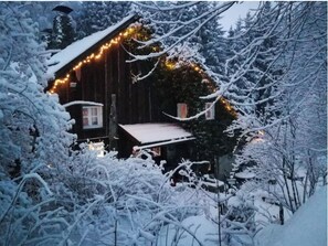 Een houten hut met een sneeuwbedekte dak en een lichtslingering langs de buitenkant.