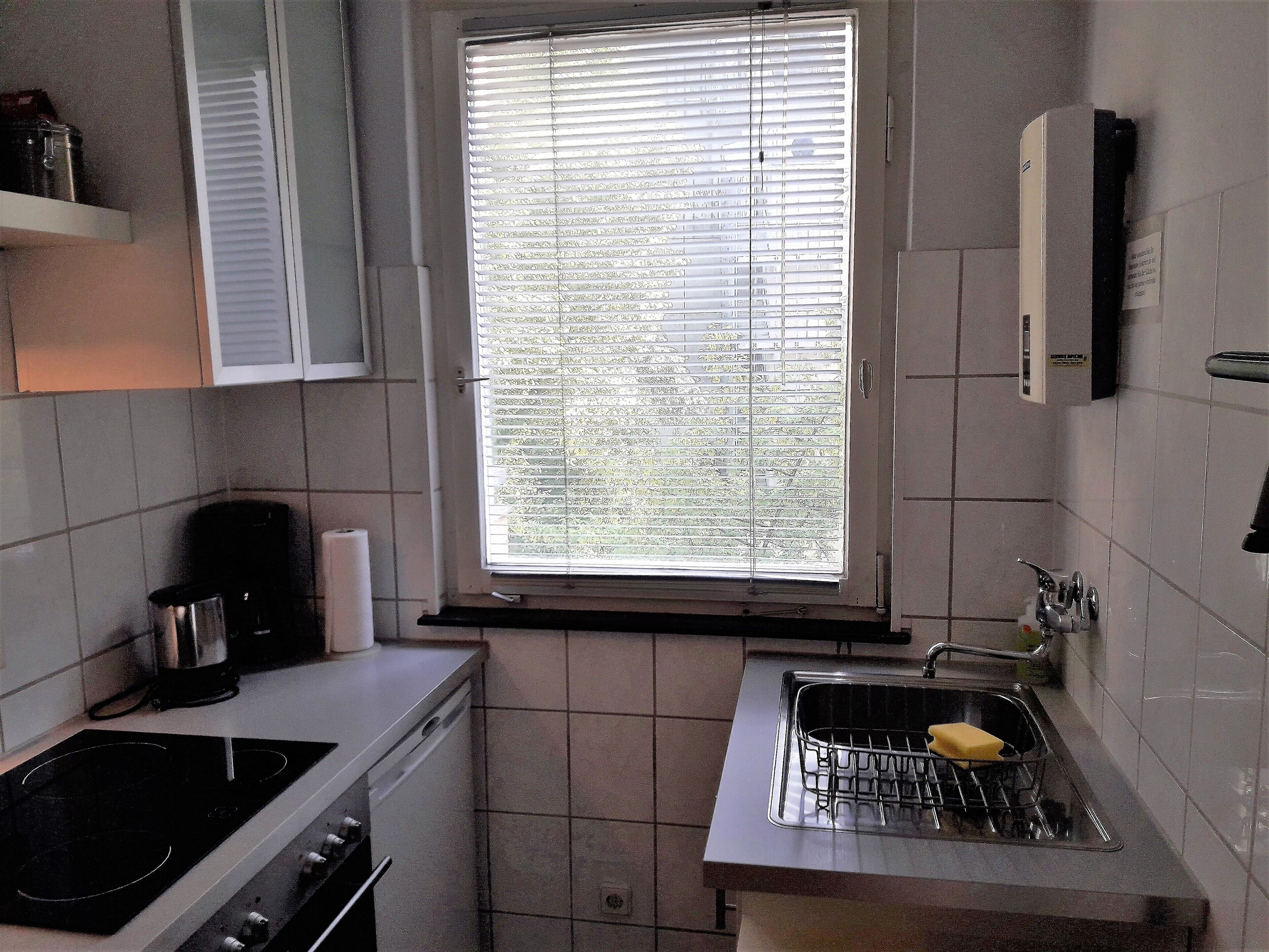Een kleine keuken met een fornuis, wastafel en raam met zonwering.