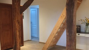 A spacious room with exposed wooden beams, a wooden staircase, and a wooden door. - Modernised farmhouse near Oldenburg with a beautiful garden in the countryside (Uplengen)