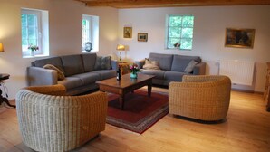 A living room with two sofas, a coffee table, and wicker chairs. - Modernised farmhouse near Oldenburg with a beautiful garden in the countryside (Uplengen)