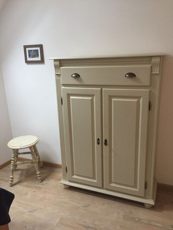 A beige wardrobe with two doors and a small stool.