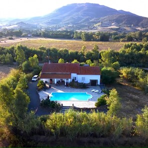 Une maison avec une piscine, entourée de verdure et avec une chaîne de montagnes en arrière-plan.