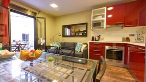 Een moderne keuken met rode kastjes, een glazen eettafel en een bank in de woonkamer.