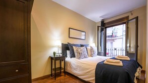 Een slaapkamer met een bed, nachtkastjes, een kledingkast en een balkon met uitzicht.