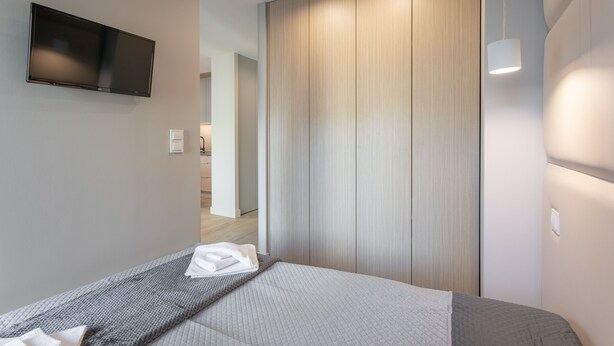 Quarto de hotel moderno com uma cama, uma TV de tela plana na parede e uma porta de madeira deslizante.